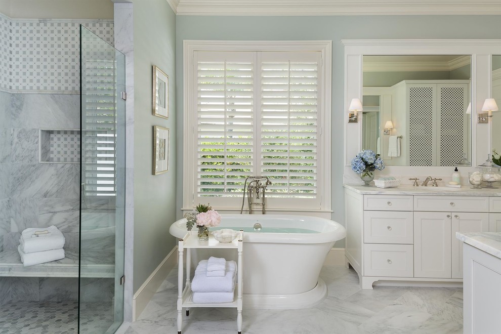 Пример оригинального дизайна: главная ванная комната в морском стиле с фасадами в стиле шейкер, белыми фасадами, отдельно стоящей ванной, серой плиткой, мраморной плиткой, синими стенами, мраморным полом, мраморной столешницей, белым полом, белой столешницей и зеркалом с подсветкой