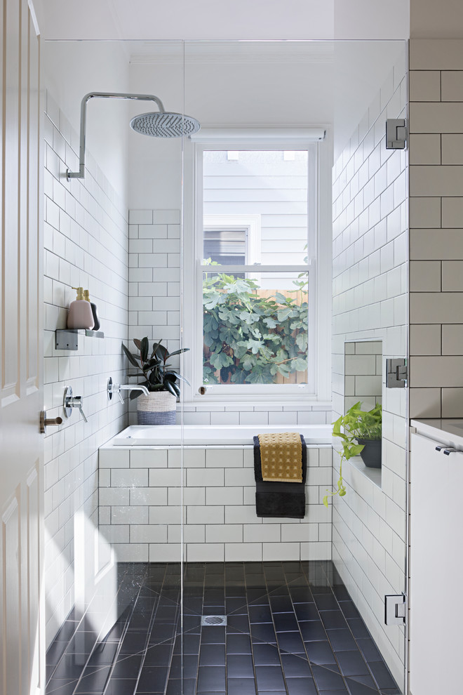 Cette image montre une salle d'eau design avec un placard à porte plane, des portes de placard blanches, une baignoire posée, un espace douche bain, un carrelage blanc, un carrelage métro, un mur blanc, un sol noir et une cabine de douche à porte battante.