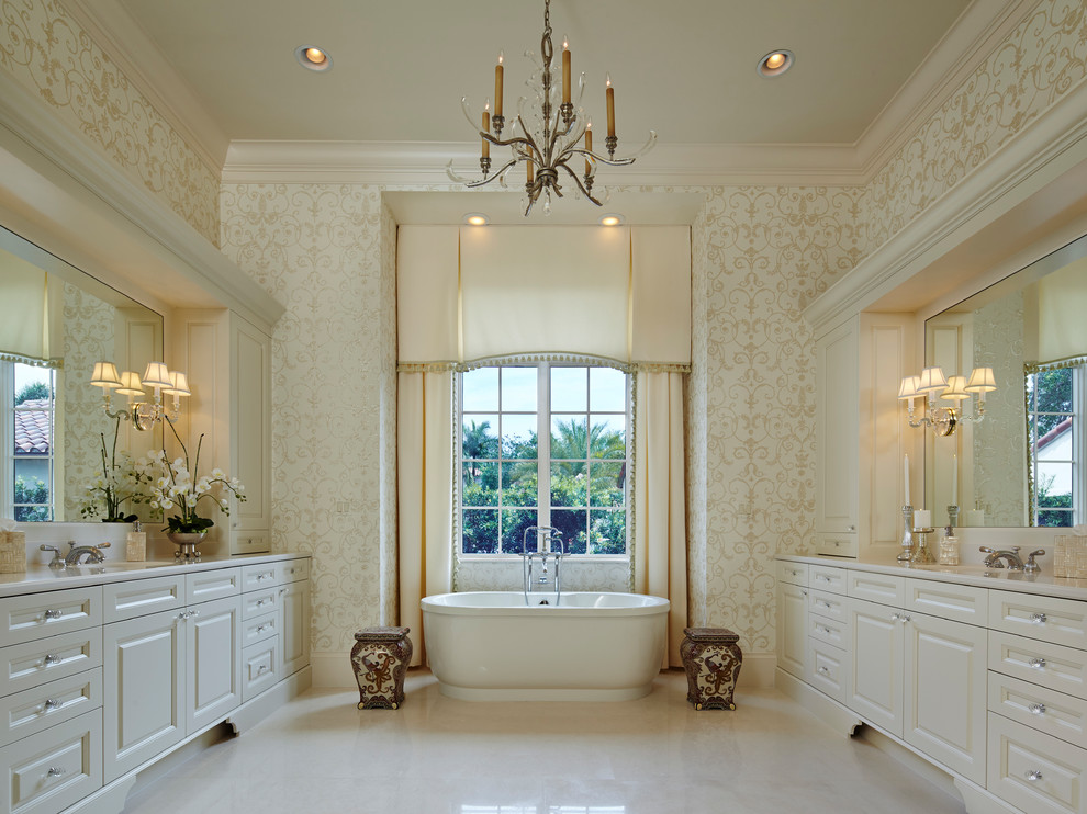 Diseño de cuarto de baño tradicional con bañera exenta, suelo de mármol, encimera de mármol, suelo blanco, armarios con paneles con relieve, puertas de armario blancas, paredes beige y aseo y ducha