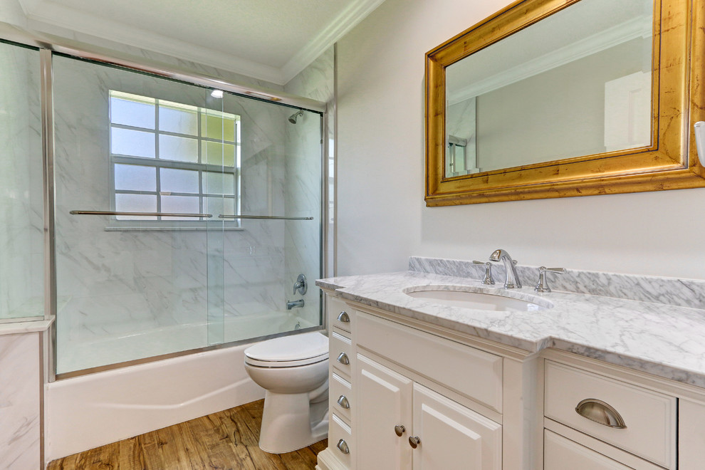 マイアミにある中くらいなトランジショナルスタイルのおしゃれなバスルーム (浴槽なし) (レイズドパネル扉のキャビネット、白いキャビネット、アルコーブ型浴槽、シャワー付き浴槽	、分離型トイレ、マルチカラーのタイル、石スラブタイル、白い壁、濃色無垢フローリング、アンダーカウンター洗面器、大理石の洗面台、茶色い床、引戸のシャワー) の写真