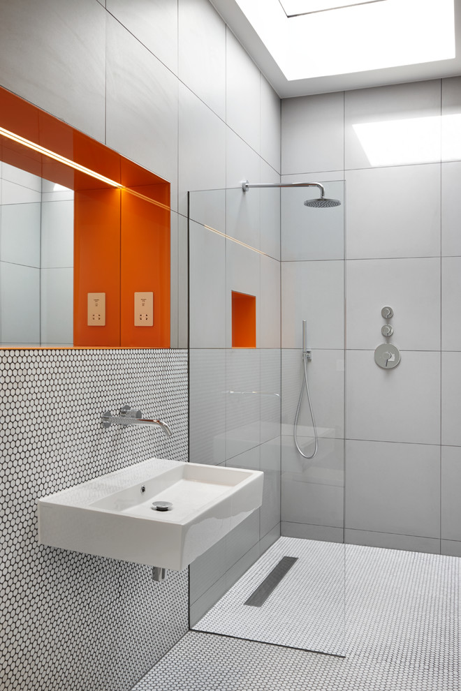Modern inredning av ett badrum, med en kantlös dusch, grå kakel, mosaikgolv, ett väggmonterat handfat, vitt golv och med dusch som är öppen