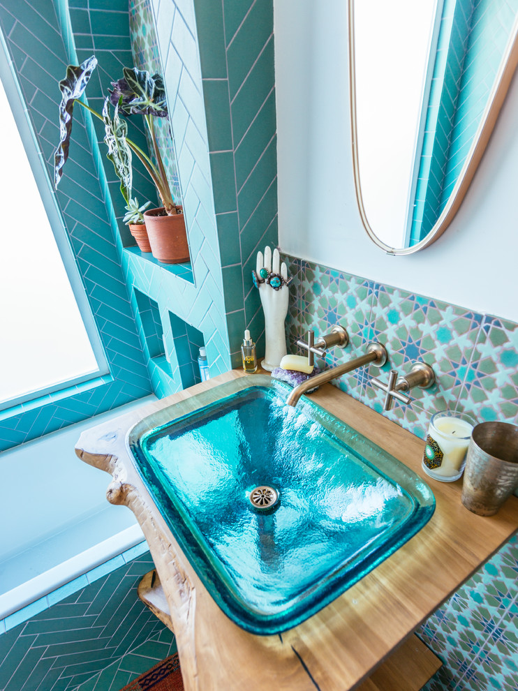 Cette image montre une salle de bain méditerranéenne avec un combiné douche/baignoire, un carrelage vert, des carreaux de céramique, un mur blanc, un sol en carrelage de céramique, un lavabo de ferme, un plan de toilette en bois, un sol vert et aucune cabine.