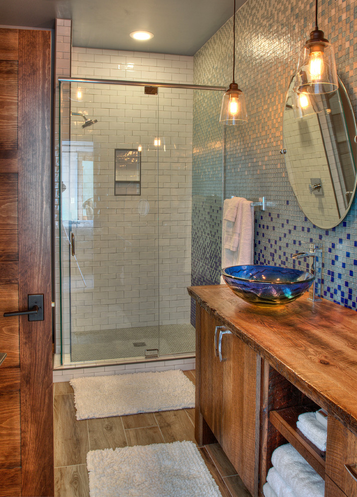 Idéer för ett rustikt badrum med dusch, med möbel-liknande, skåp i mellenmörkt trä, en dusch i en alkov, en toalettstol med separat cisternkåpa, blå kakel, glaskakel, blå väggar, cementgolv, ett fristående handfat, träbänkskiva, brunt golv och dusch med gångjärnsdörr