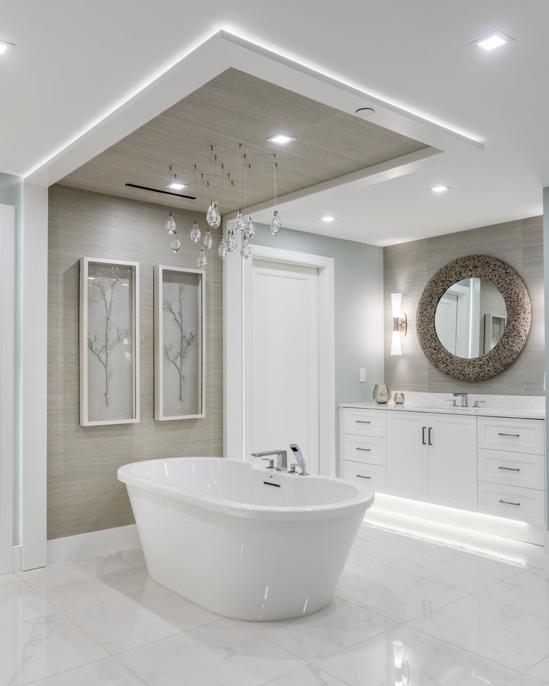 Aménagement d'une salle de bain classique avec un placard à porte shaker, des portes de placard blanches, une baignoire indépendante, un mur gris, un lavabo encastré, un sol blanc et un plan de toilette blanc.