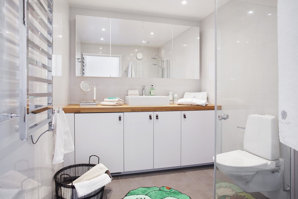 Inredning av ett minimalistiskt mellanstort en-suite badrum, med ett fristående handfat, släta luckor, vita skåp, träbänkskiva, en hörndusch, en vägghängd toalettstol, tunnelbanekakel, vita väggar och klinkergolv i keramik