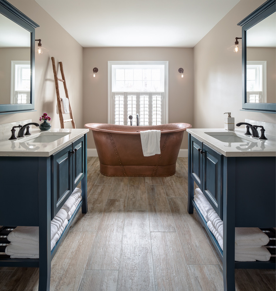 Inspiration for a traditional bathroom in Portland Maine with blue cabinets, a freestanding bath, beige walls, a submerged sink, brown floors, white worktops and raised-panel cabinets.