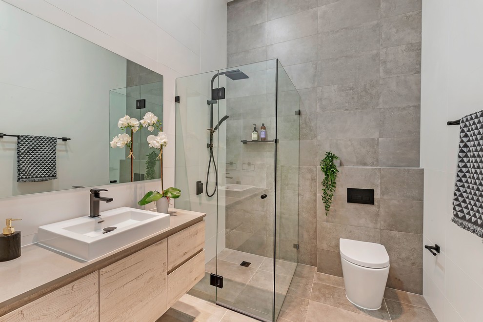 Modernes Duschbad mit flächenbündigen Schrankfronten, hellen Holzschränken, Eckdusche, Toilette mit Aufsatzspülkasten, grauen Fliesen, weißer Wandfarbe, Einbauwaschbecken, beigem Boden, Falttür-Duschabtrennung und beiger Waschtischplatte in Sydney