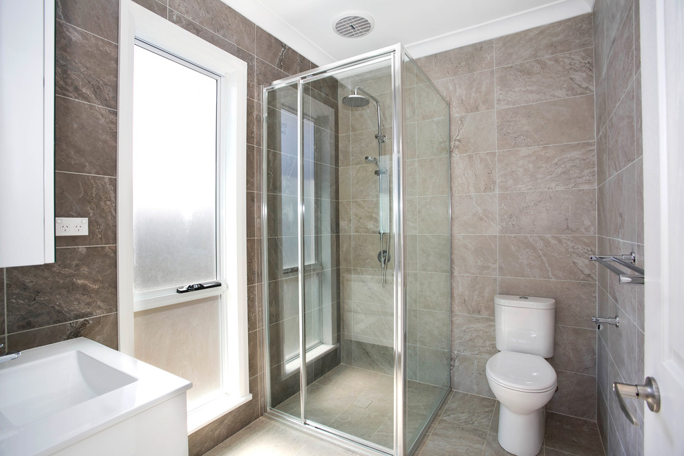 Photo of a classic bathroom in Sydney with flat-panel cabinets, white cabinets, a corner shower, a two-piece toilet, brown tiles, stone tiles, brown walls, an integrated sink, brown floors and a hinged door.