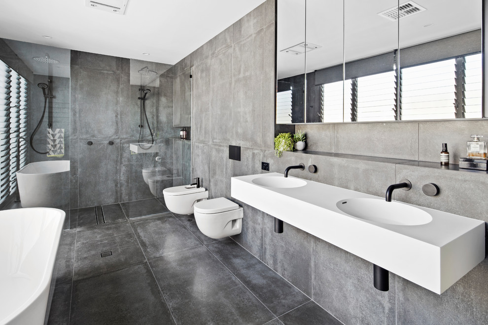 Foto de cuarto de baño contemporáneo con bañera exenta, ducha doble, sanitario de pared, baldosas y/o azulejos grises, paredes grises, aseo y ducha, lavabo integrado, suelo gris, ducha abierta y encimeras blancas