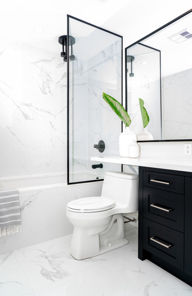 Cette image montre une salle d'eau design de taille moyenne avec un placard à porte shaker, des portes de placard noires, une baignoire en alcôve, un combiné douche/baignoire, WC à poser, un carrelage blanc, un sol blanc, un plan de toilette blanc, un mur blanc, un sol en marbre et un lavabo encastré.