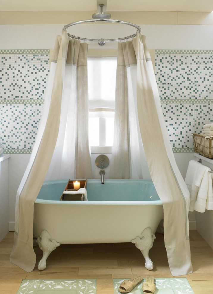 Bild på ett lantligt badrum, med ett badkar med tassar, flerfärgad kakel, mosaik och ljust trägolv