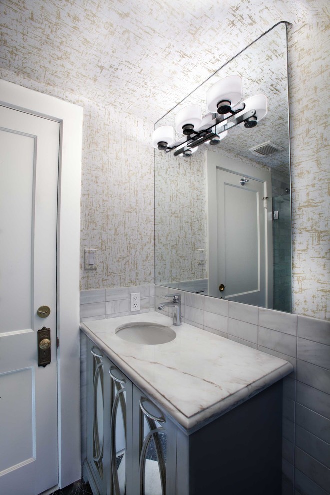 Diseño de cuarto de baño contemporáneo pequeño con puertas de armario grises, combinación de ducha y bañera, sanitario de dos piezas, baldosas y/o azulejos grises, paredes grises, suelo de mármol, encimera de mármol, lavabo bajoencimera, armarios tipo mueble y bañera empotrada