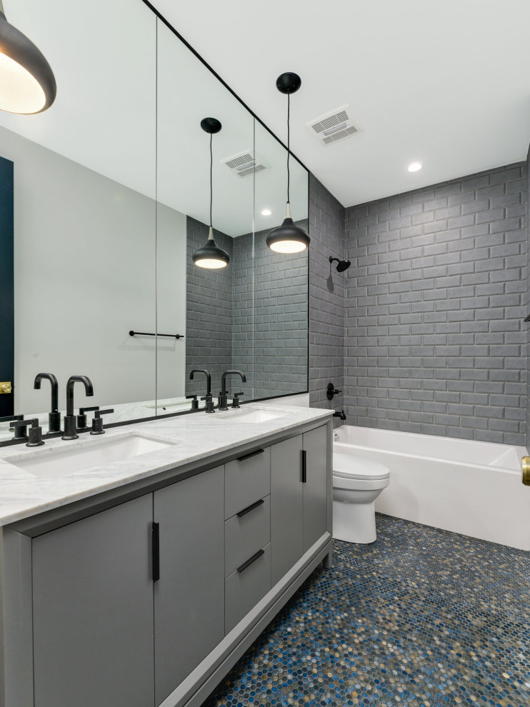На фото: ванная комната в современном стиле с плоскими фасадами, серыми фасадами, ванной в нише, душем над ванной, серой плиткой, серыми стенами, полом из мозаичной плитки, врезной раковиной, разноцветным полом, открытым душем, белой столешницей, тумбой под две раковины и встроенной тумбой с