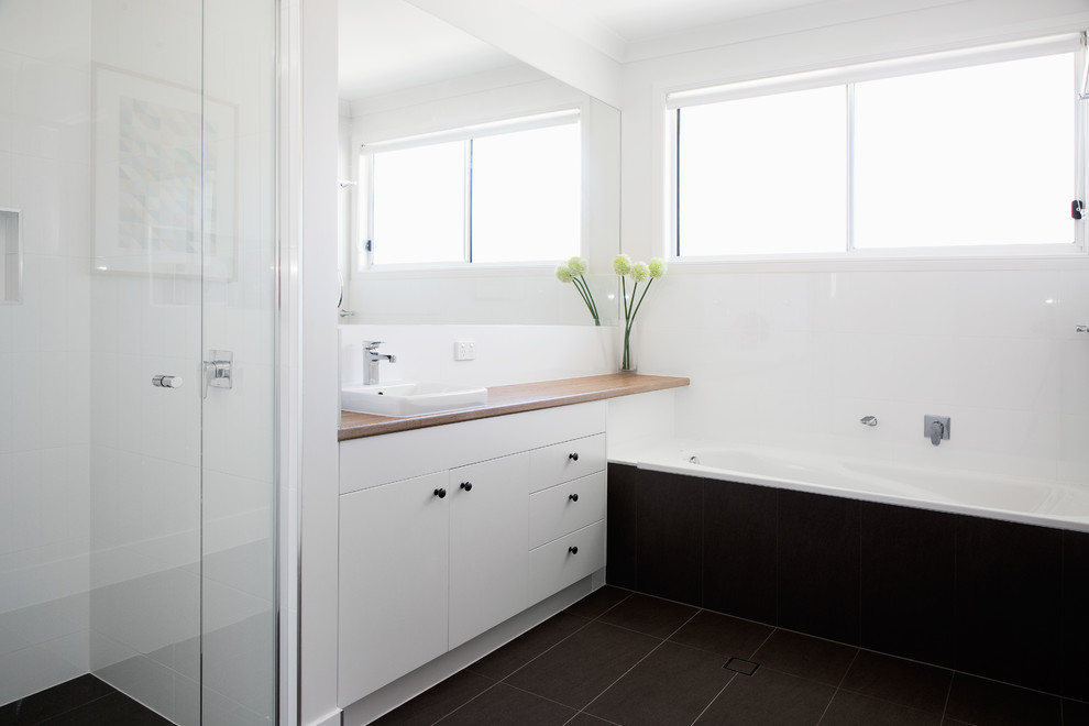 Идея дизайна: главная ванная комната среднего размера в современном стиле с плоскими фасадами, белыми фасадами, накладной ванной, душем в нише, раздельным унитазом, белой плиткой, керамической плиткой, белыми стенами, полом из керамической плитки, накладной раковиной, столешницей из искусственного кварца, черным полом, душем с распашными дверями и белой столешницей