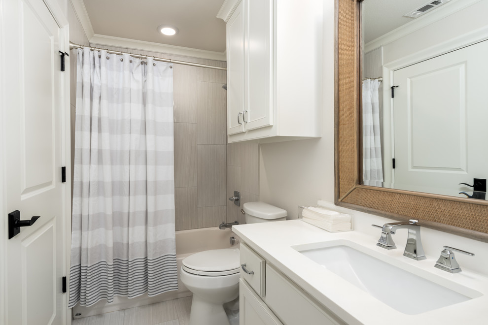Cette image montre une salle d'eau traditionnelle avec un placard à porte shaker, des portes de placard blanches, une baignoire posée, un combiné douche/baignoire, WC à poser, un carrelage gris, des carreaux de porcelaine, un mur blanc, un sol en carrelage de porcelaine, un lavabo encastré, un plan de toilette en quartz, un sol gris et une cabine de douche avec un rideau.