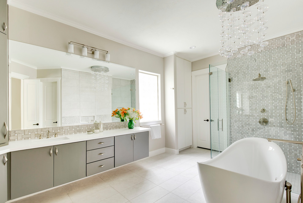 Cette image montre une salle de bain design avec un placard à porte plane, des portes de placard grises, une baignoire indépendante, une douche d'angle, un carrelage gris, un mur beige, un lavabo encastré, un sol beige, une cabine de douche à porte battante et un plan de toilette blanc.