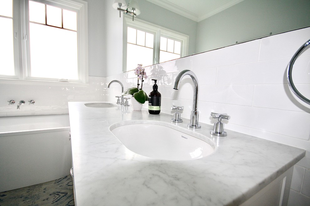 Inredning av ett klassiskt mellanstort en-suite badrum, med skåp i shakerstil, vita skåp, ett fristående badkar, en öppen dusch, en vägghängd toalettstol, vit kakel, porslinskakel, vita väggar, klinkergolv i porslin, ett undermonterad handfat, marmorbänkskiva, vitt golv och med dusch som är öppen