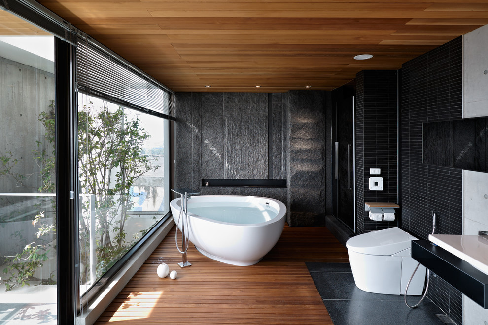 Modernes Badezimmer En Suite mit freistehender Badewanne, schwarzen Fliesen, braunem Holzboden und Toilette mit Aufsatzspülkasten in Sonstige