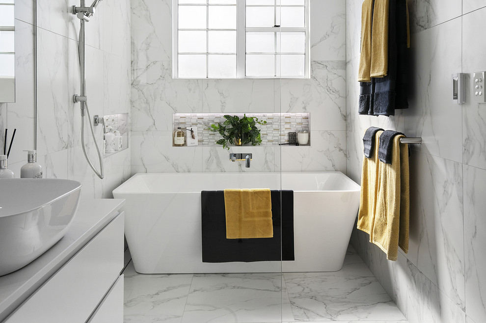 Пример оригинального дизайна: большая главная ванная комната в современном стиле с фасадами островного типа, белыми фасадами, отдельно стоящей ванной, душевой комнатой, раздельным унитазом, черно-белой плиткой, керамической плиткой, белыми стенами, полом из керамической плитки, настольной раковиной, мраморной столешницей, белым полом, открытым душем и белой столешницей