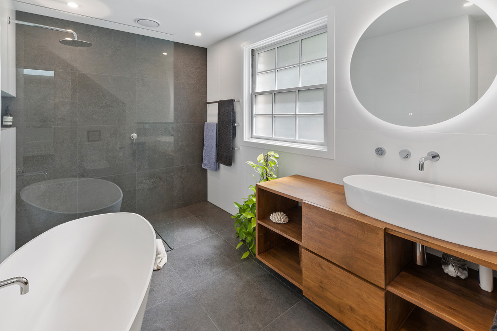 Exempel på ett mellanstort modernt brun brunt en-suite badrum, med ett fristående badkar, porslinskakel, vita väggar, klinkergolv i porslin, ett fristående handfat, träbänkskiva, grått golv, med dusch som är öppen, släta luckor, skåp i mellenmörkt trä, en kantlös dusch och grå kakel