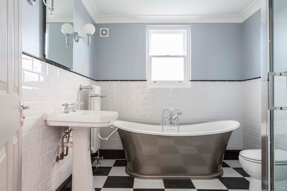 Klassisches Badezimmer mit freistehender Badewanne, schwarzen Fliesen, weißen Fliesen, blauer Wandfarbe und Sockelwaschbecken in Sonstige