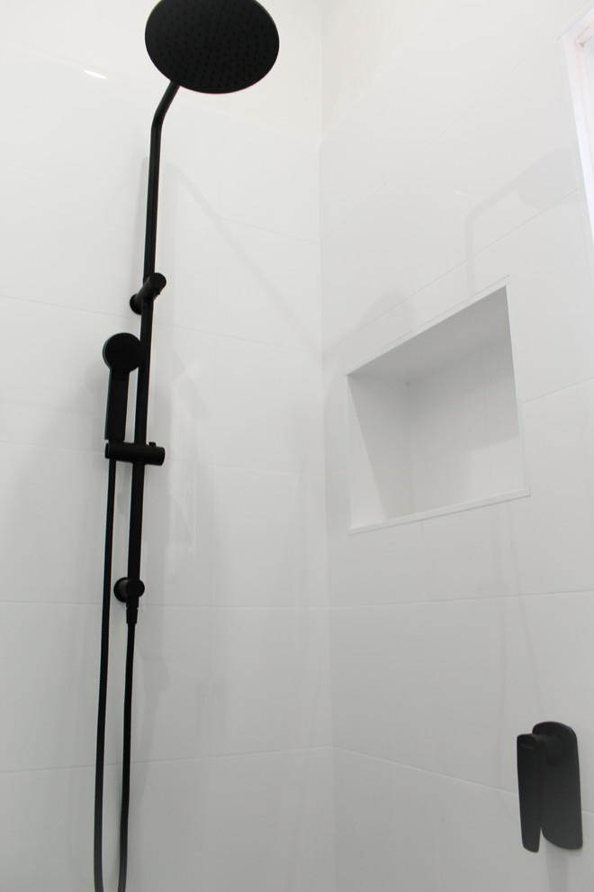 Klassisk inredning av ett litet en-suite badrum, med möbel-liknande, skåp i mörkt trä, våtrum, en toalettstol med hel cisternkåpa, vit kakel, keramikplattor, vita väggar, klinkergolv i porslin, ett integrerad handfat, bänkskiva i akrylsten, grått golv och med dusch som är öppen
