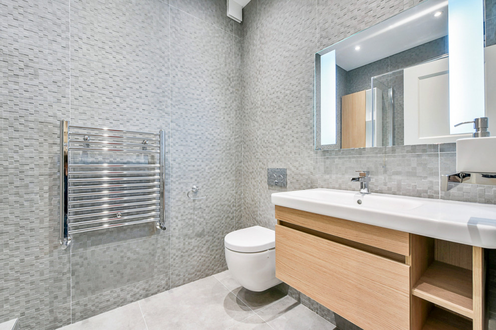Small contemporary bathroom in London with flat-panel cabinets, light wood cabinets, a wall mounted toilet, grey tiles, ceramic tiles, grey walls, porcelain flooring, a wall-mounted sink, grey floors and a hinged door.