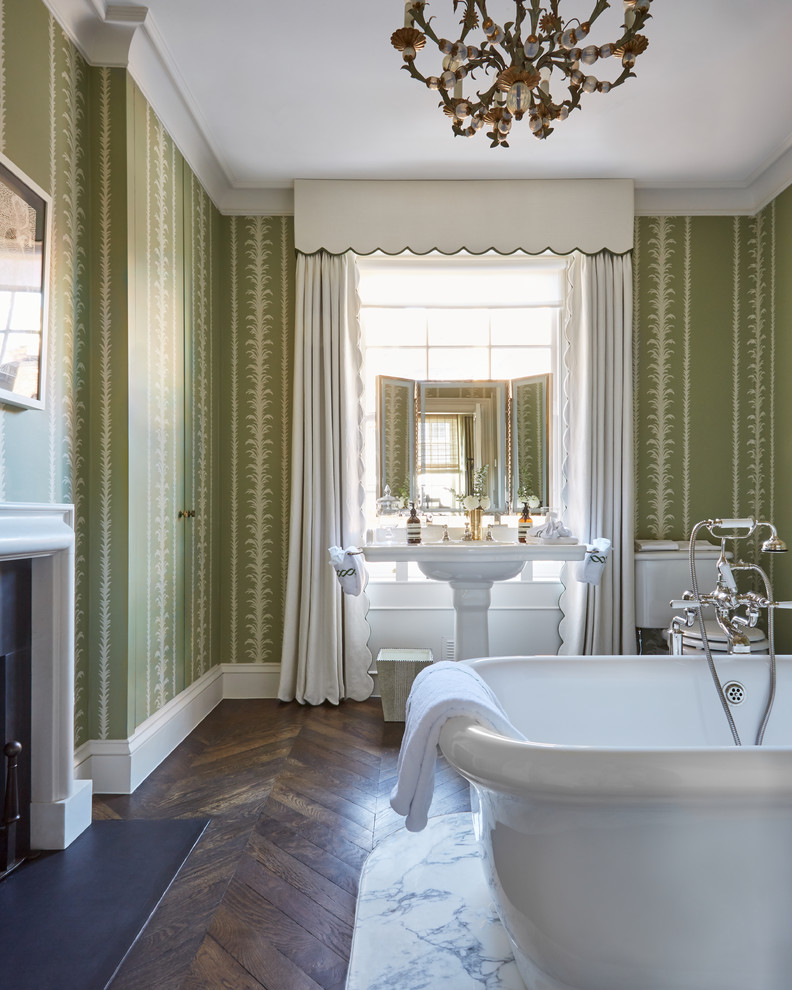Klassisches Badezimmer mit freistehender Badewanne, grüner Wandfarbe, braunem Holzboden, Sockelwaschbecken und braunem Boden in London