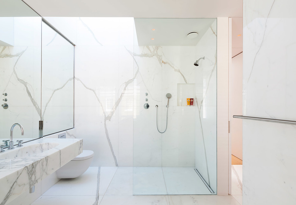 Example of a mid-sized trendy 3/4 marble tile and black and white tile marble floor and white floor bathroom design in London with a wall-mount toilet, white walls, a wall-mount sink, marble countertops and a niche