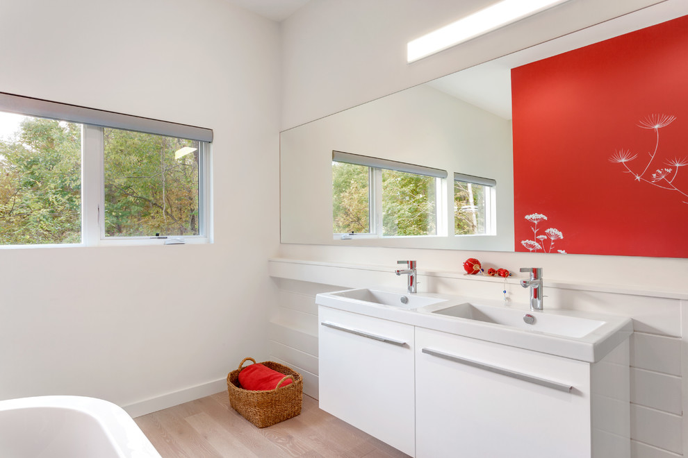 Photo of a medium sized modern ensuite bathroom in Bridgeport with flat-panel cabinets, white cabinets, a freestanding bath, red walls, light hardwood flooring, an integrated sink, solid surface worktops, grey floors and white worktops.