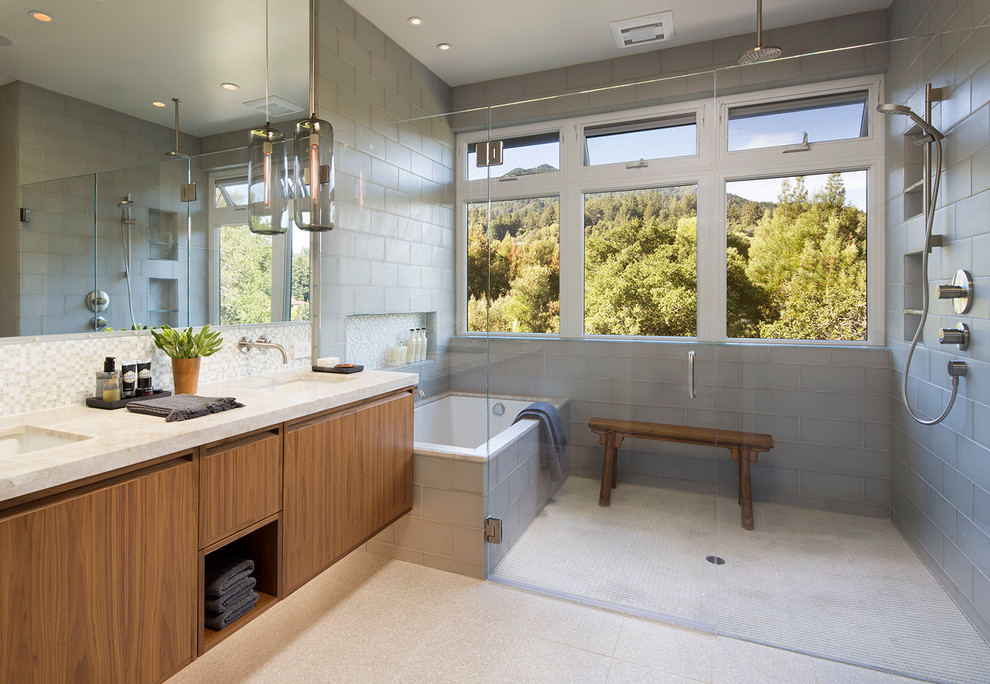 Photo of a contemporary ensuite bathroom in San Francisco with flat-panel cabinets, medium wood cabinets, a built-in bath, a built-in shower, a one-piece toilet, grey tiles, glass tiles, ceramic flooring, a submerged sink and marble worktops.