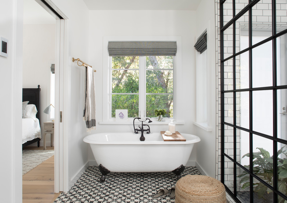 Inredning av ett lantligt badrum, med ett badkar med tassar, vit kakel, vita väggar, cementgolv och flerfärgat golv
