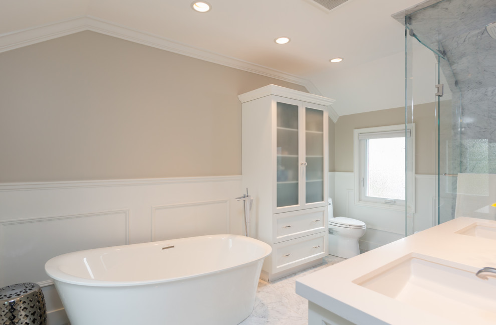 This is an example of a large traditional ensuite bathroom in Vancouver with a submerged sink, shaker cabinets, white cabinets, engineered stone worktops, a freestanding bath, a corner shower, a one-piece toilet, white tiles, stone tiles, beige walls and marble flooring.