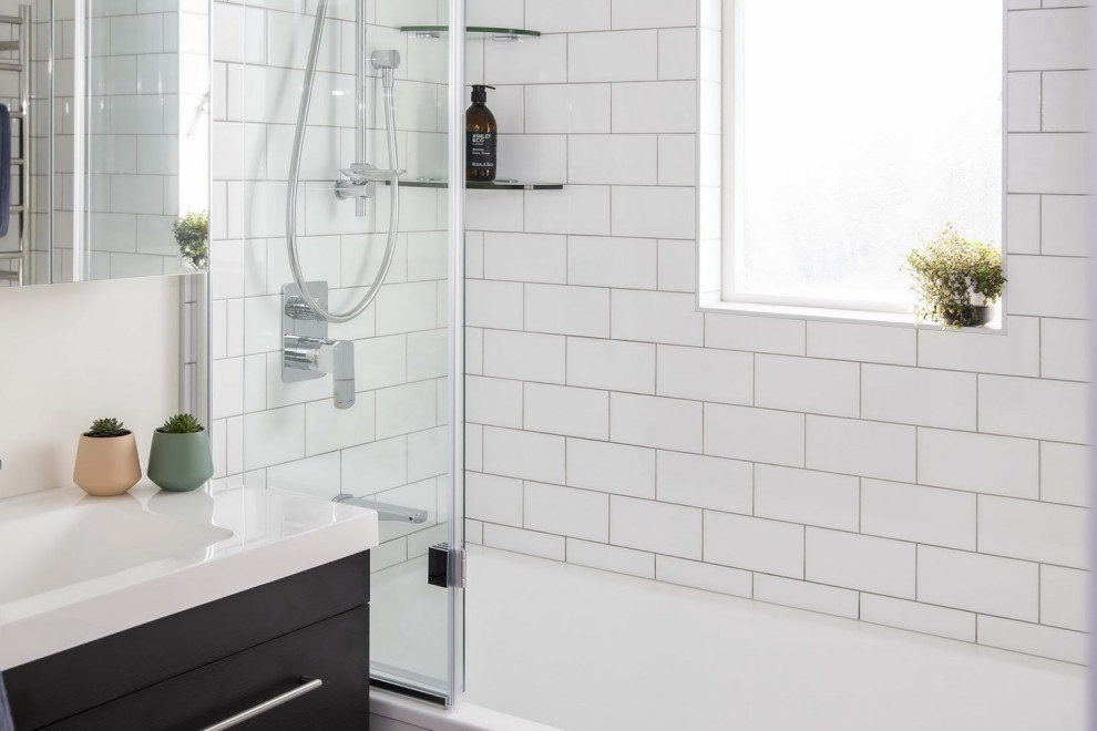 Photo of a medium sized traditional ensuite bathroom in Auckland with freestanding cabinets, brown cabinets, a built-in bath, a shower/bath combination, a two-piece toilet, white tiles, porcelain tiles, white walls, medium hardwood flooring, an integrated sink, solid surface worktops, brown floors, a hinged door, white worktops, a single sink and a floating vanity unit.