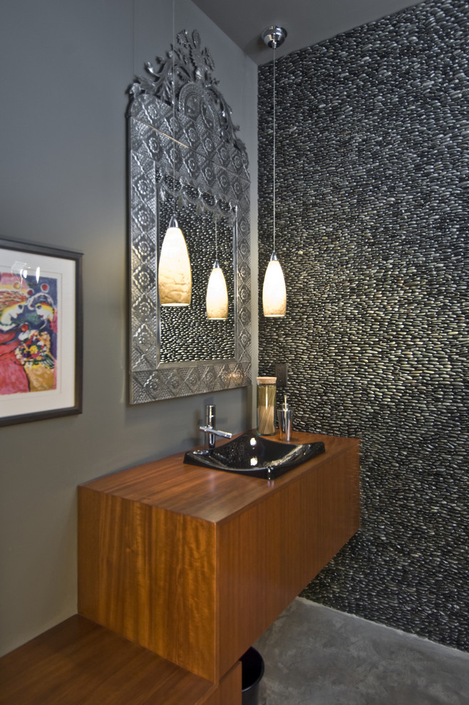 Idée de décoration pour une petite salle d'eau minimaliste en bois brun avec une vasque, un placard à porte plane, un plan de toilette en bois, un carrelage gris, une plaque de galets, un mur gris et sol en béton ciré.