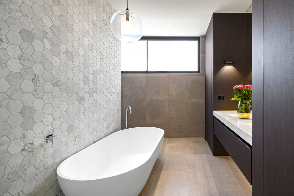 На фото: главная ванная комната в современном стиле с плоскими фасадами, темными деревянными фасадами, отдельно стоящей ванной, серыми стенами и врезной раковиной с