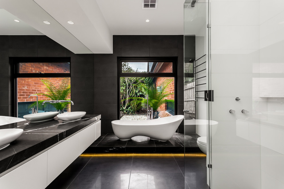 Идея дизайна: большая главная ванная комната в современном стиле с настольной раковиной, плоскими фасадами, белыми фасадами, отдельно стоящей ванной, угловым душем, черным полом и черной столешницей