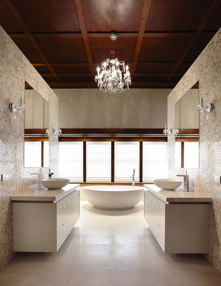 Пример оригинального дизайна: огромная главная ванная комната в классическом стиле с настольной раковиной, мраморной столешницей, бежевой плиткой, плиткой мозаикой, бежевыми стенами, белыми фасадами, отдельно стоящей ванной, бежевым полом, бежевой столешницей, подвесной тумбой и деревянным потолком