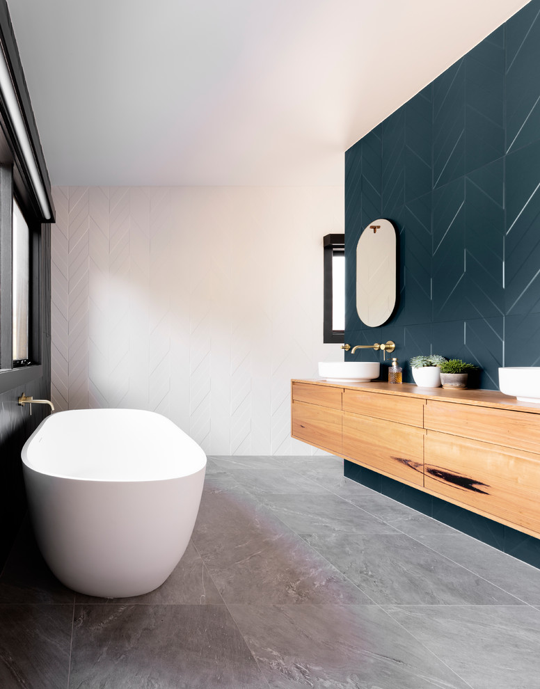 Modernes Badezimmer mit flächenbündigen Schrankfronten, hellbraunen Holzschränken, freistehender Badewanne, blauen Fliesen, Aufsatzwaschbecken, Waschtisch aus Holz, grauem Boden und brauner Waschtischplatte in Melbourne
