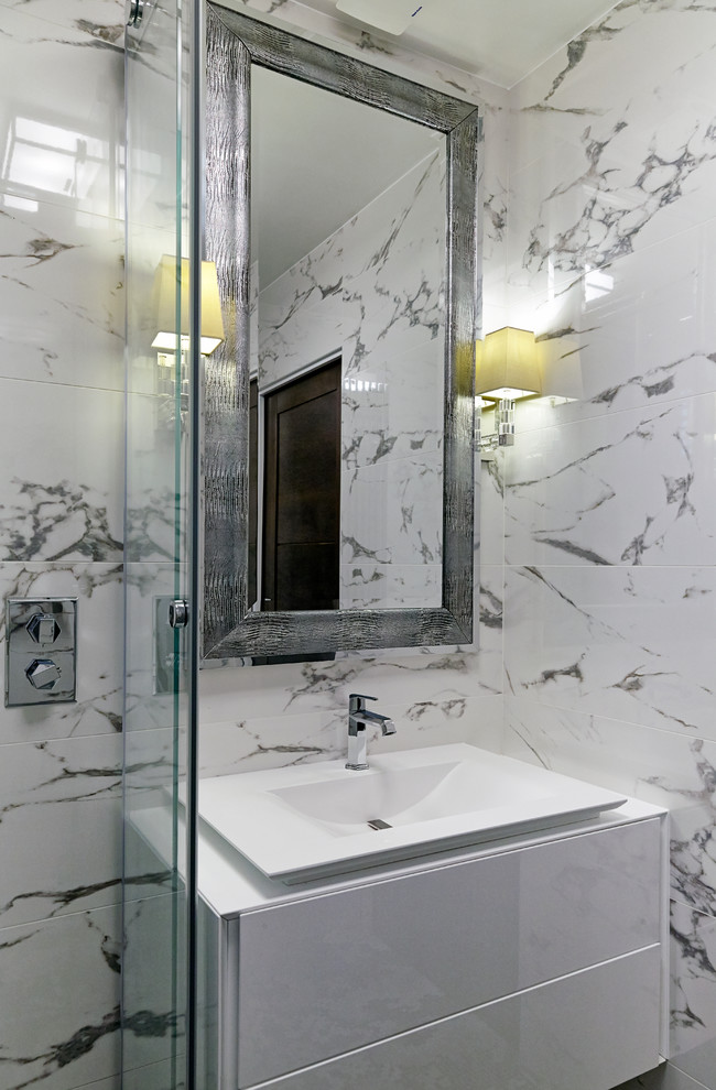 This is an example of a small contemporary ensuite bathroom in London with flat-panel cabinets, white cabinets, a corner shower, white tiles, marble tiles, white walls, a built-in sink, solid surface worktops and a sliding door.