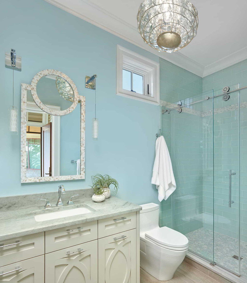 Foto på ett maritimt grå badrum med dusch, med beige skåp, en dusch i en alkov, en toalettstol med hel cisternkåpa, blå kakel, tunnelbanekakel, blå väggar, ett undermonterad handfat, marmorbänkskiva, beiget golv, dusch med skjutdörr och luckor med infälld panel