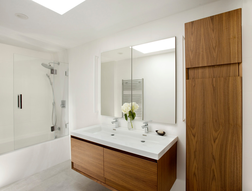 Inspiration for a medium sized modern family bathroom in Boston with flat-panel cabinets, medium wood cabinets, an alcove bath, a shower/bath combination, white tiles, porcelain tiles, white walls, porcelain flooring, a trough sink, grey floors, a hinged door, white worktops, an enclosed toilet, double sinks and a floating vanity unit.