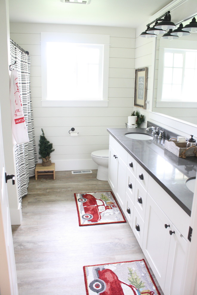 Cette image montre une salle de bain rustique de taille moyenne avec un placard à porte shaker, des portes de placard blanches, une baignoire posée, un combiné douche/baignoire, WC à poser, un mur blanc, un sol en vinyl, un lavabo encastré et un plan de toilette en quartz modifié.