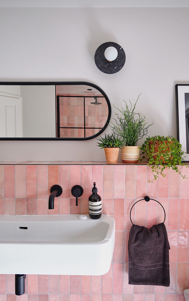 Foto på ett mellanstort funkis badrum för barn, med svarta skåp, en öppen dusch, en vägghängd toalettstol, rosa kakel, keramikplattor, vita väggar, terrazzogolv, ett avlångt handfat, svart golv och med dusch som är öppen