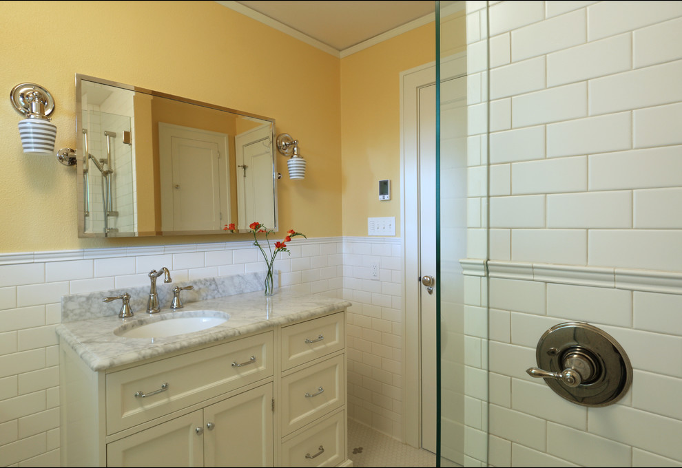 Immagine di una piccola stanza da bagno con doccia chic con lavabo sottopiano, ante in stile shaker, ante bianche, top in marmo, piastrelle bianche, piastrelle in ceramica, pareti gialle e pavimento con piastrelle in ceramica