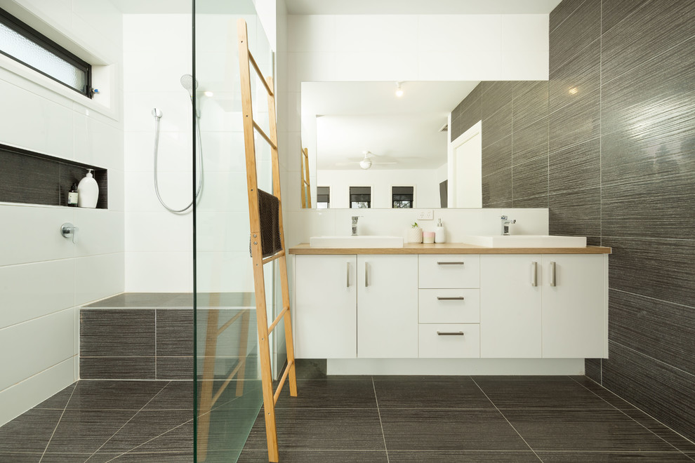 Cette image montre une salle de bain design avec un placard à porte plane, des portes de placard blanches, un carrelage gris, un lavabo posé, un plan de toilette en bois, un sol gris et un plan de toilette beige.