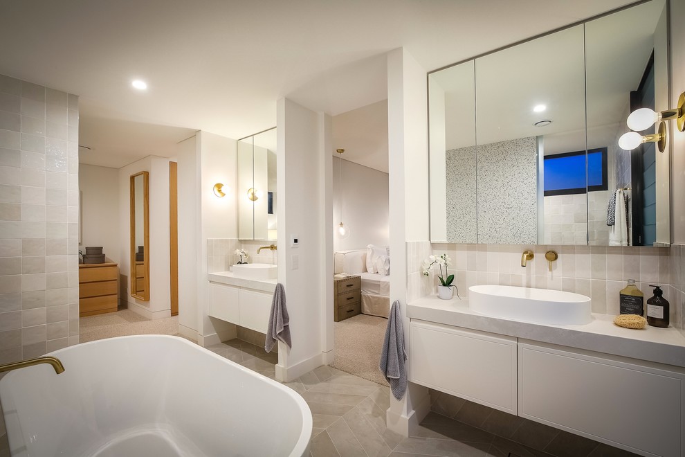 На фото: главная ванная комната в современном стиле с белыми фасадами, отдельно стоящей ванной, серой плиткой, белыми стенами, настольной раковиной, серым полом, серой столешницей и плоскими фасадами