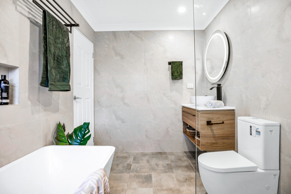 Design ideas for a medium sized contemporary ensuite bathroom in Sydney with light wood cabinets, a freestanding bath, a corner shower, a two-piece toilet, grey tiles, marble tiles, beige walls, ceramic flooring, a vessel sink, engineered stone worktops, grey floors, an open shower, white worktops, a wall niche, a single sink and a floating vanity unit.