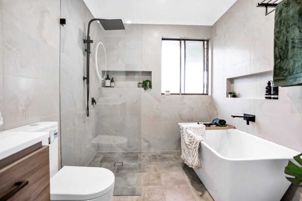 Пример оригинального дизайна: главная ванная комната среднего размера в современном стиле с светлыми деревянными фасадами, отдельно стоящей ванной, угловым душем, раздельным унитазом, серой плиткой, мраморной плиткой, бежевыми стенами, полом из керамической плитки, настольной раковиной, столешницей из искусственного кварца, серым полом, открытым душем, белой столешницей, нишей, тумбой под одну раковину и подвесной тумбой