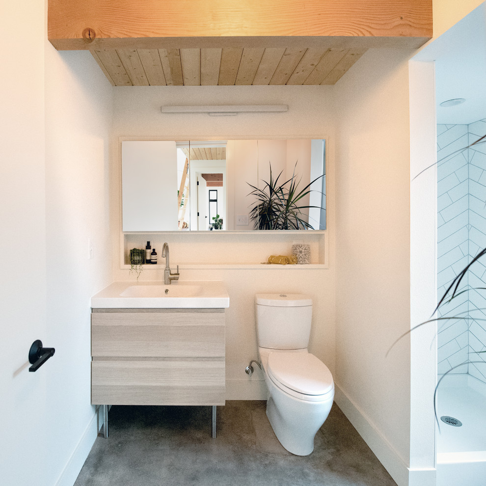 Idéer för att renovera ett funkis gul gult badrum, med släta luckor, skåp i ljust trä, en dusch i en alkov, en toalettstol med separat cisternkåpa, vit kakel, keramikplattor, vita väggar, betonggolv, ett integrerad handfat, grått golv och dusch med duschdraperi